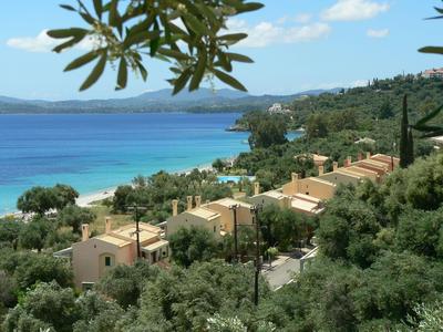Coastal hotel with sandy beach, blue sea, and green vegetation in the background.