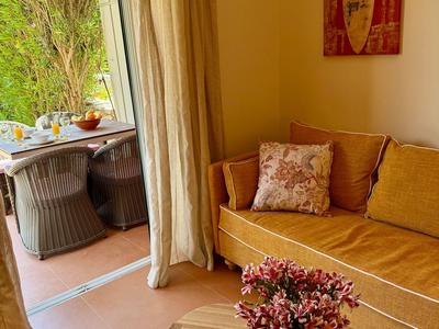 Cozy hotel balcony with sofa, table, and view of garden with green bushes.