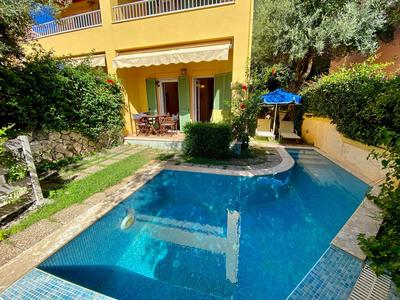 Private pool in front of a yellow vacation house with terrace and garden.
