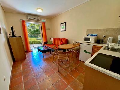 Small living room with kitchenette, red sofa, wooden furniture, and terrace door in hotel room.