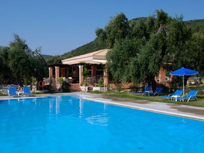 Large hotel pool with blue water, surrounded by lounge chairs and green trees under clear sky.
