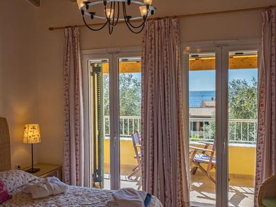 Bright hotel room with double bed, balcony, and sea view in daylight.