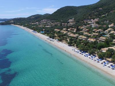 Long sandy beach with clear blue water, umbrellas, and green hills in the background.