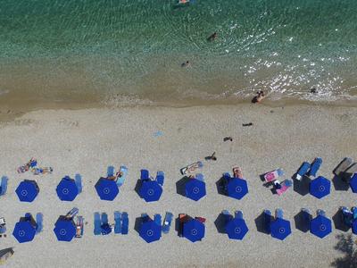 Aerial view of a beach with blue umbrellas and people by clear water.