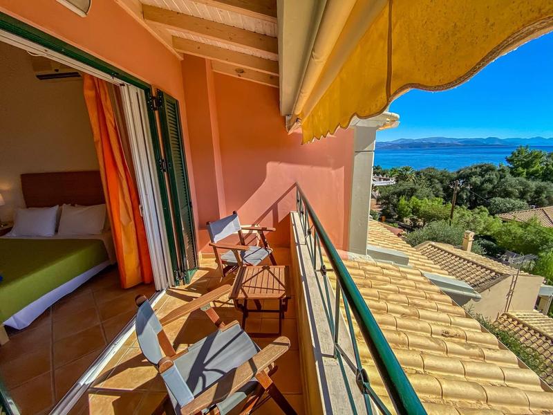 Balkon mit Stühlen, orangener Wand, Dachterrasse und Blick auf Meer und grüne Landschaft.
