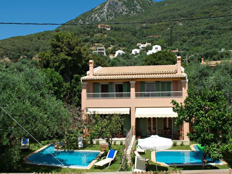 Zweistöckiges Haus mit Terrakottadach, zwei Pools und üppigem Grün vor bewaldetem Berg.