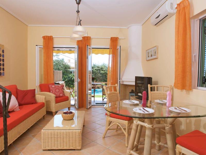 Helles Wohnzimmer mit orangen Vorhängen, roten Sofas, Glastisch und Blick auf Terrasse.