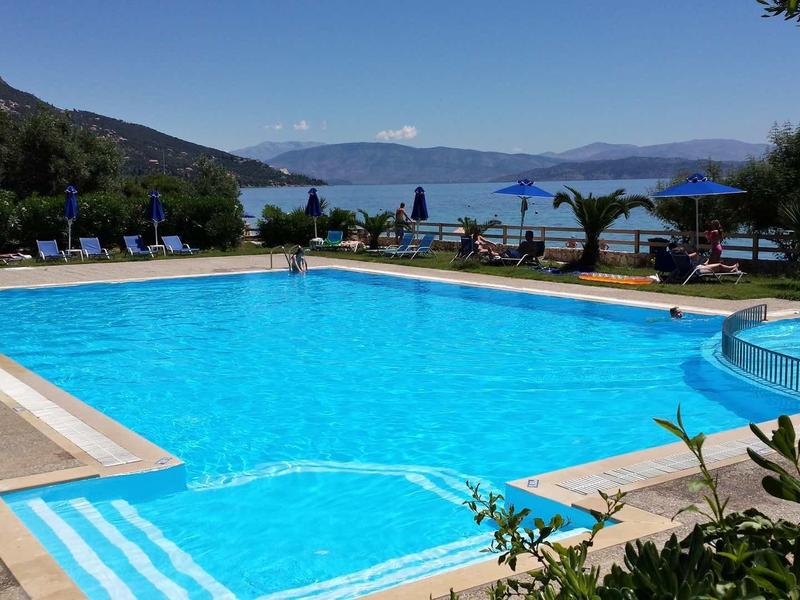 Großer rechteckiger Pool mit blauem Wasser, umgeben von Sonnenschirmen, Palmen und Bergen im Hintergrund.