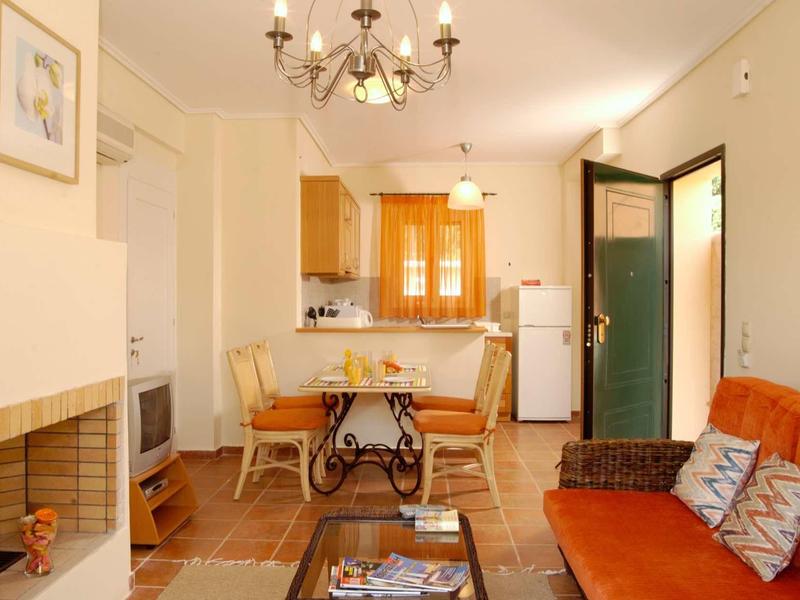 Gemütliches Wohnzimmer mit orangenem Sofa, Holztisch, Kamin und offener Küche mit Esstisch.