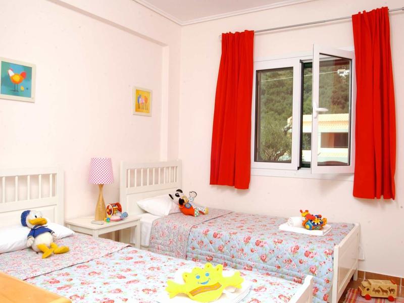 Kinderzimmer mit zwei Einzelbetten, roten Vorhängen und bunten Wandbildern, helle Wände.