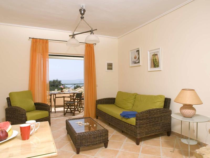 Helles Wohnzimmer mit Rattansofa, grün-gelben Kissen, Sessel, Glastisch und orangenen Vorhängen.