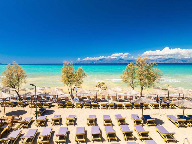 Strand mit Liegen unter Sonnenschirmen, blaues Meer und Himmel im Hintergrund.