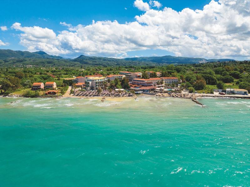 Hotelanlage am Strand mit türkisfarbenem Meer und bewölktem Himmel im Hintergrund.