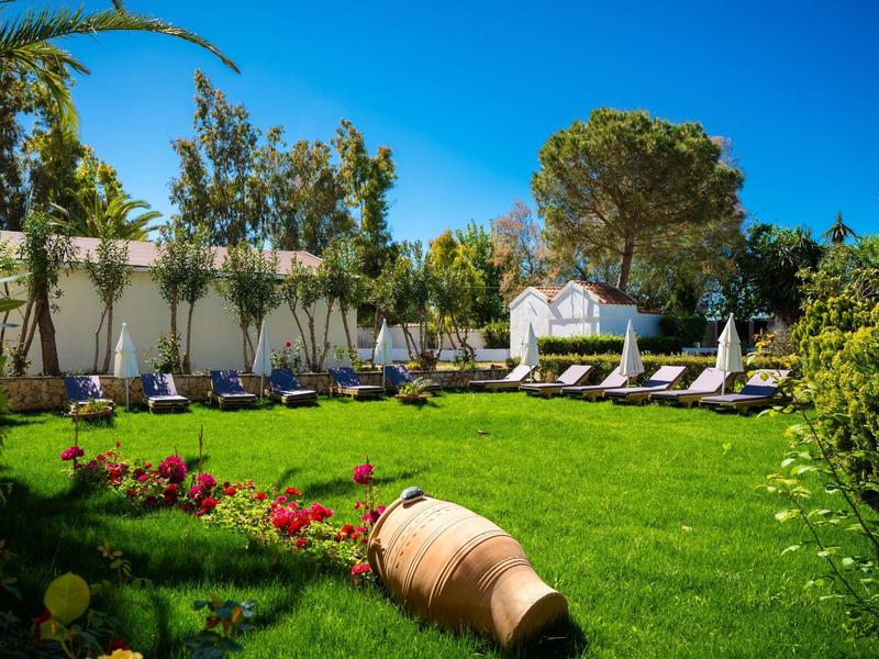 Grüner Garten mit Liegestühlen unter blauem Himmel in einem Hotelgarten.