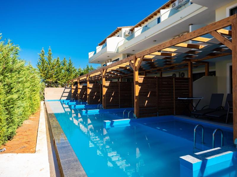 Moderner Außenpool mit Pergola und Liegestühlen neben einem Wohngebäude bei Sonnenschein.