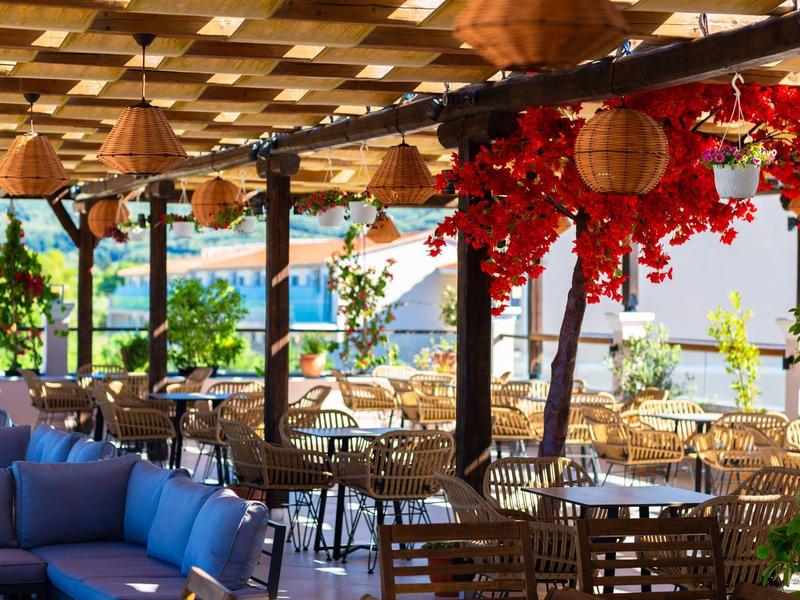 Überdachte Außenterrasse eines Restaurants mit Holztischen, Stühlen und blauer Sofaecke.