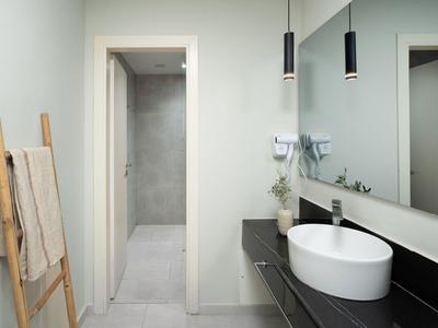 Modernes Badezimmer mit weißem Waschbecken, schwarzer Ablage und Holzwäscheleiter an heller Wand.