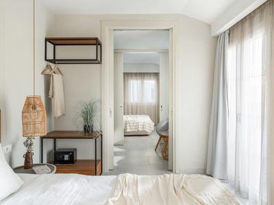 Helles Schlafzimmer mit weißer Bettwäsche, Holzmöbeln und großem Spiegel, daneben Gardinen.