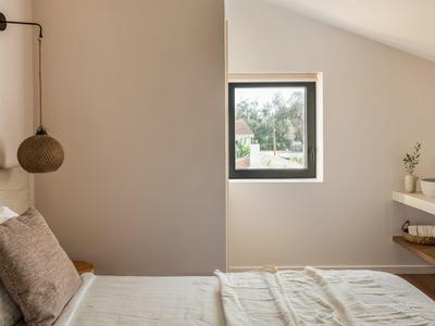 Helles Schlafzimmer mit schräger Wand, kleinem Fenster, Bettenrand, modernen Regalen und Hängeleuchte.