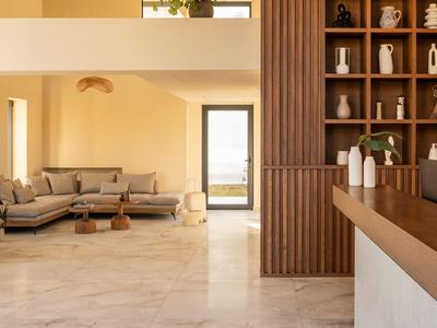 Area soggiorno moderna con divano angolare grigio, tavolo in legno e scaffalature aperte in tonalità calde.