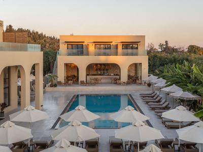 Piscina moderna dell'hotel con lettini, ombrelloni e edificio su due piani sullo sfondo.
