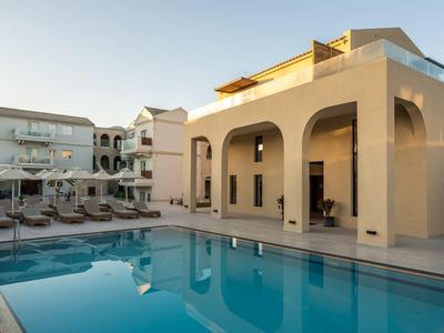 Complesso alberghiero moderno con piscina, lettini e edifici beige-bianco al tramonto.