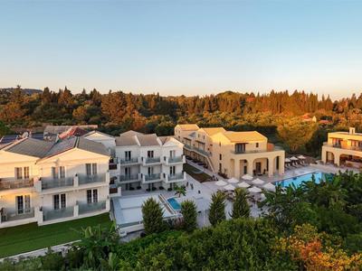 Grande hotel con più edifici e piscina, circondato da alberi al tramonto.