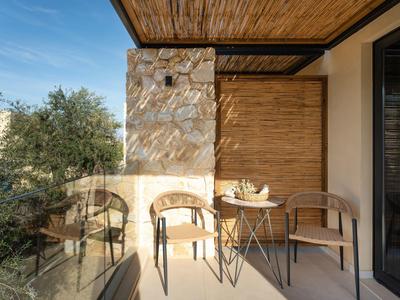 Gemütliche Terrasse mit zwei Holzmöbeln, kleinem runden Tisch und natürlicher Steinwand.