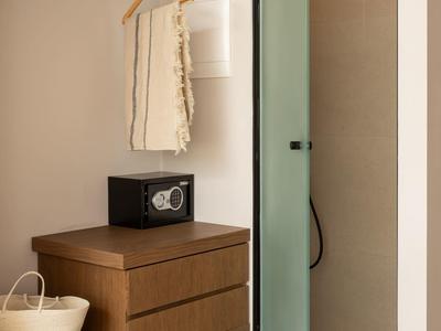 Kompakter begehbarer Kleiderschrank mit Holzmöbeln, Safe, Regal und angrenzender Dusche hinter Glastür.