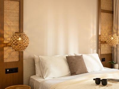 Camera d'hotel accogliente con letto matrimoniale, biancheria bianca e lampada da parete in legno decorativa.