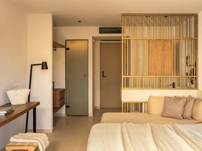 Helles Schlafzimmer mit großem Bett, Holzmöbeln, Federkissen und goldfarbenem Raumteiler.