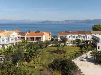 Vista di edifici bianchi con tetti rossi, giardino e mare blu chiaro sullo sfondo.