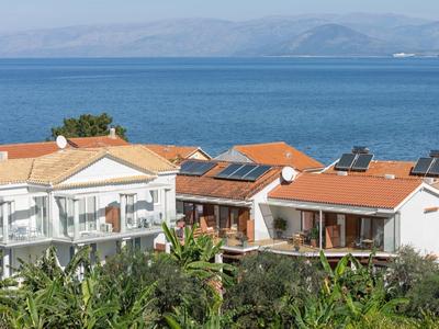 Diverse case con tetti di tegole rosse davanti al mare blu e una riva verde.