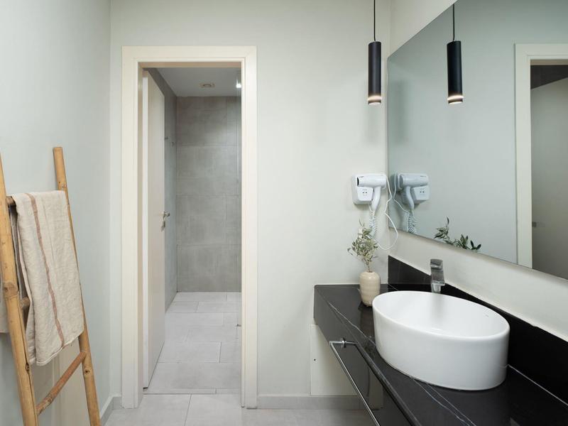 Modernes Badezimmer mit weißem Waschbecken, schwarzer Ablage und Holzwäscheleiter an heller Wand.