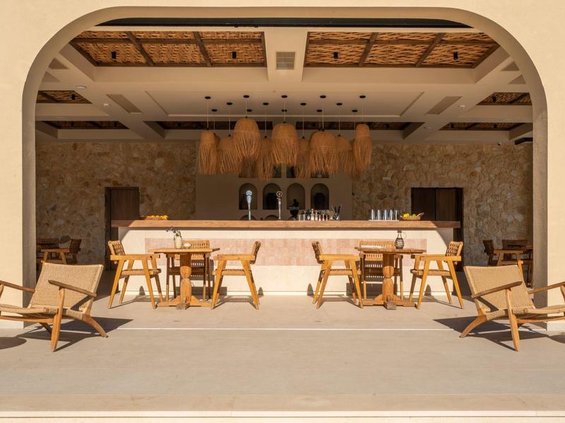 Offene Bar mit Holzstühlen, Tischen und Sandboden in warmem, natürlichem Farbschema.