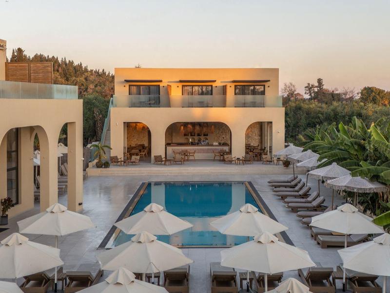 Moderner Hotelpool mit Liegestühlen und Sonnenschirmen, zwei Gebäude mit Arkaden im Abendlicht.