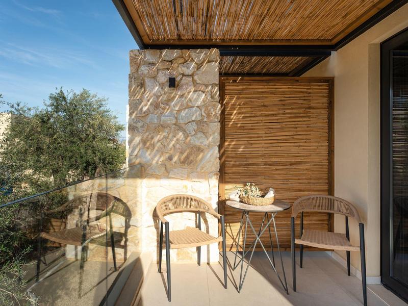Gemütliche Terrasse mit zwei Holzmöbeln, kleinem runden Tisch und natürlicher Steinwand.