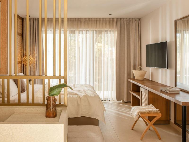 Helles Schlafzimmer mit Balkon, Vorhängen, Holzmöbeln und TV an der Wand.