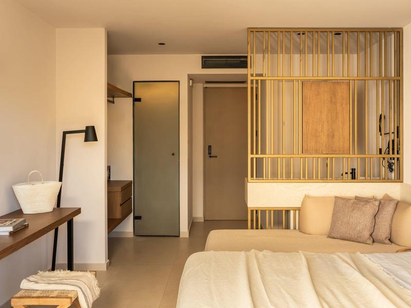 Helles Schlafzimmer mit großem Bett, Holzmöbeln, Federkissen und goldfarbenem Raumteiler.