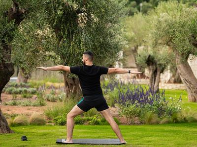 Personne pratiquant le yoga en plein air sur un tapis entourée d'arbres et d'herbe verte.