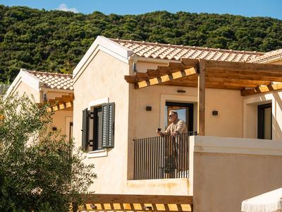 Maison avec terrasse et pergola en bois devant une colline boisée sous un ciel clair