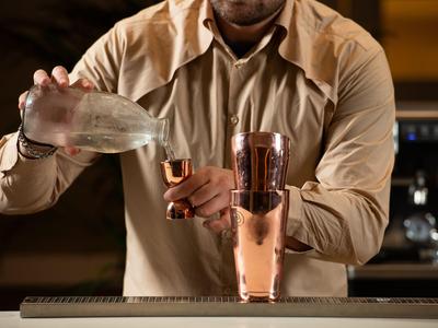 Barman verse un liquide clair d'un pichet dans un doseur derrière un bar.