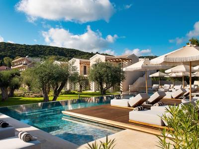 Luxuriöser Poolbereich mit Sonnenliegen und Sonnenschirmen vor einem Hotel in mediterraner Landschaft.