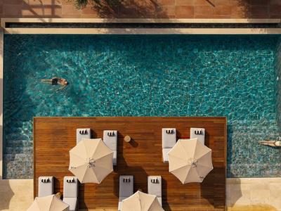 Vue de dessus d'une piscine avec terrasse en bois et parasols, entourée de chaises longues.
