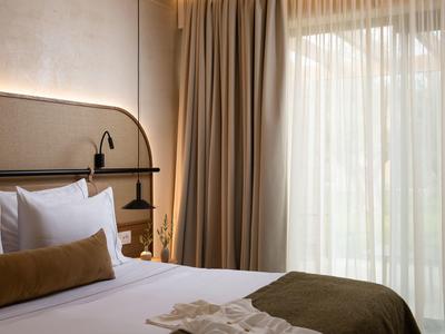 Gemütliches Hotelzimmer mit großem Bett, weißen Kissen und Vorhängen vor einem Fenster.