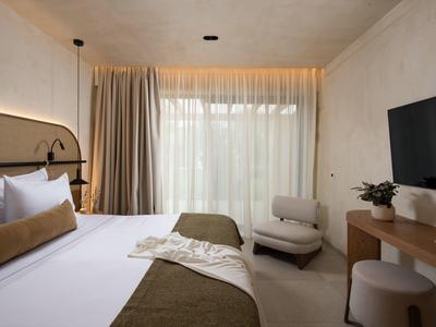 Helles Hotelzimmer mit großem Bett, Fernseher an der Wand und bequemen Sitzgelegenheiten.