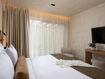 Modernes Hotelzimmer mit großem Bett, Fernseher und bodentiefen Fenstern mit Vorhängen.