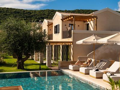 Maison de vacances moderne avec terrasse, piscine et plusieurs parasols dans un cadre verdoyant.