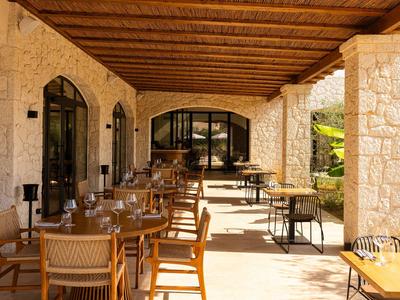 Terrasse couverte avec poutres en bois, colonnes en pierre et tables dressées avec des chaises.