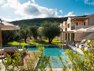 Piscine extérieure luxueuse avec transats et parasols devant un hôtel dans un paysage verdoyant.